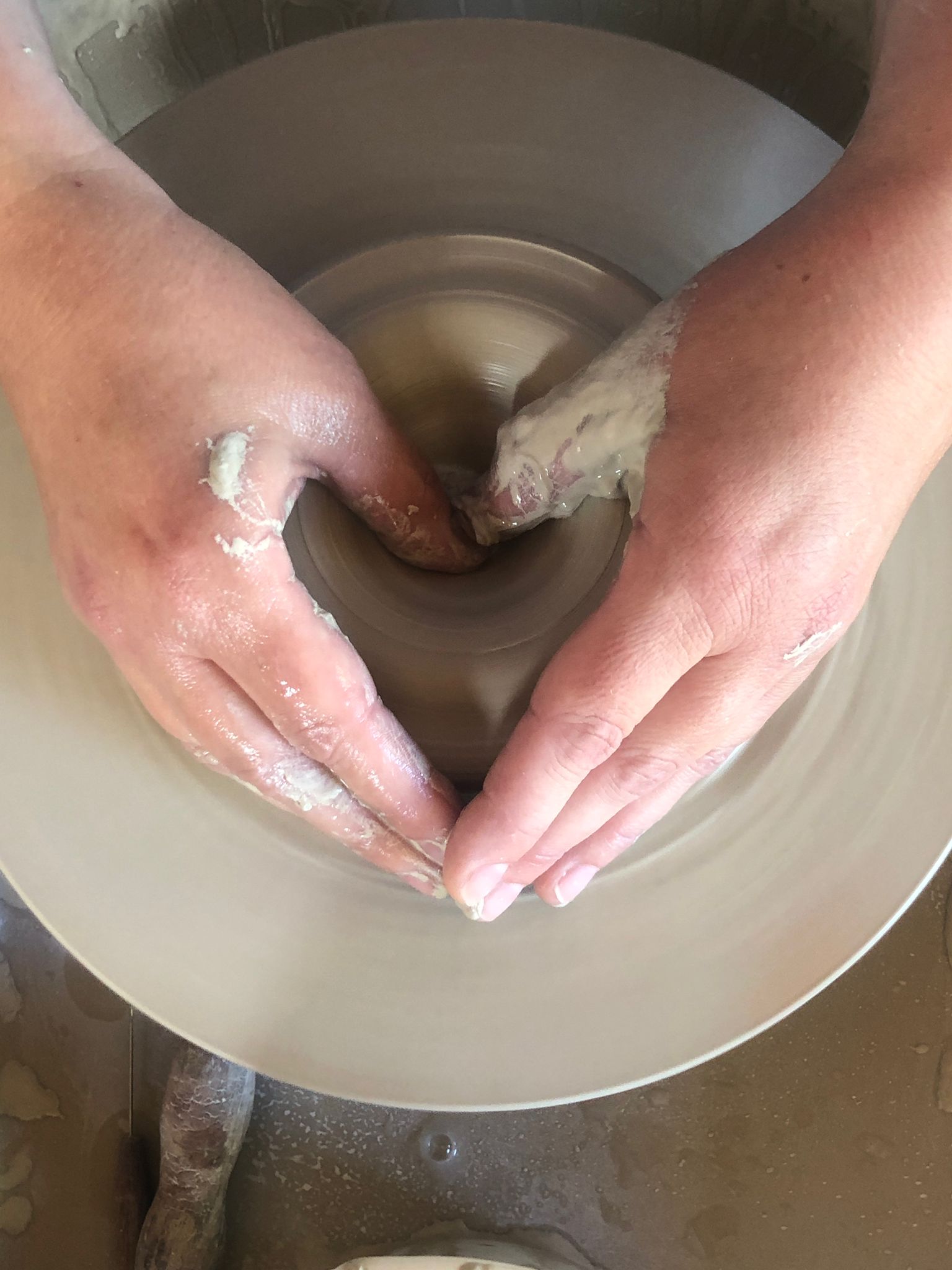 Hands shaping clay on the pottery wheel